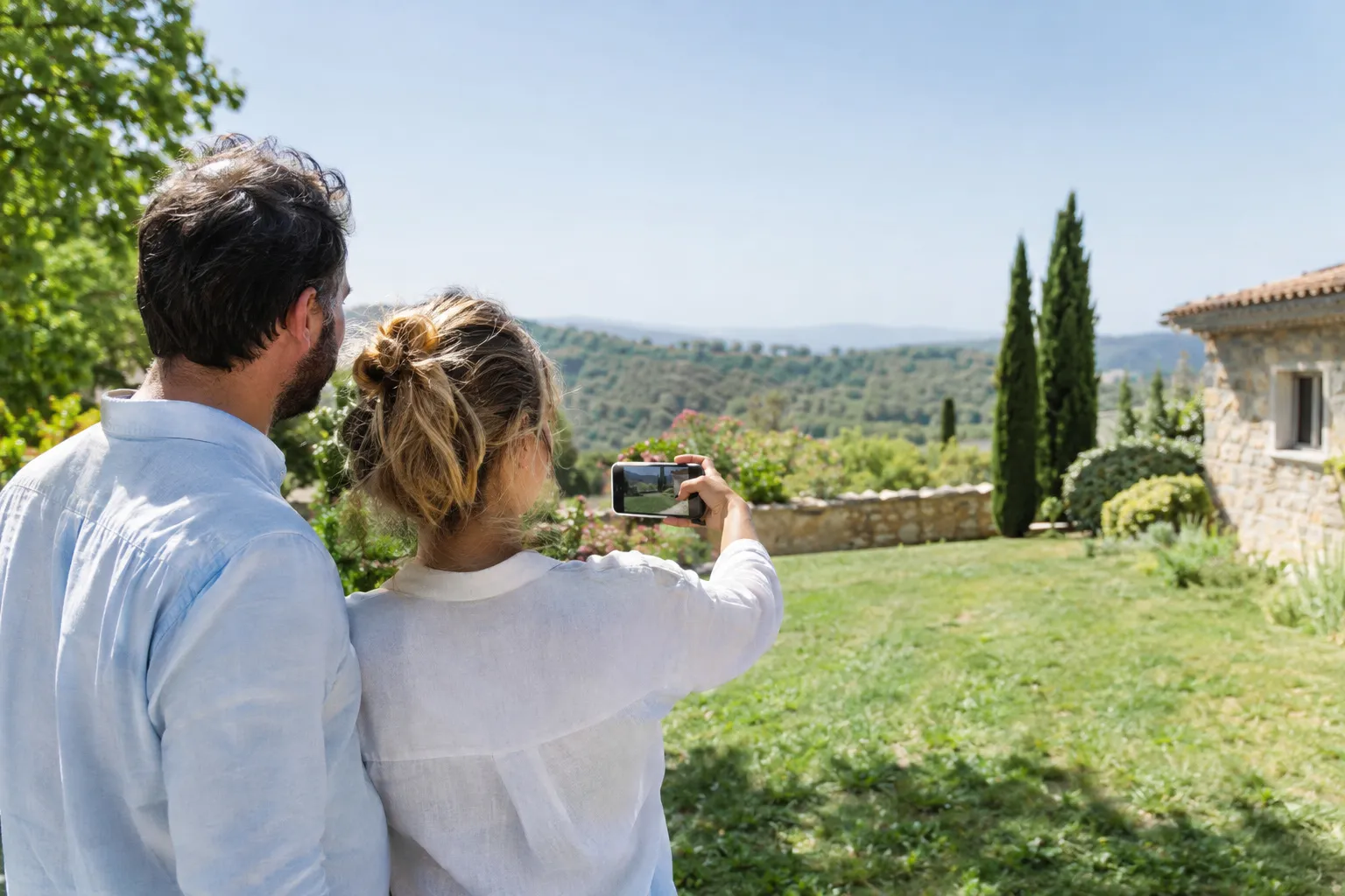 Un couple photographie son jardin avec un téléphone pour demander un devis de piscine